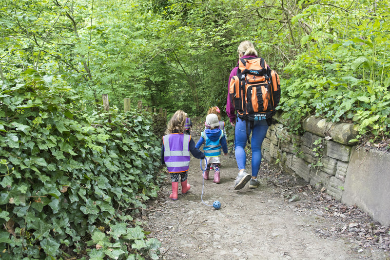 Two small children walking a woodland path ahead of an adult