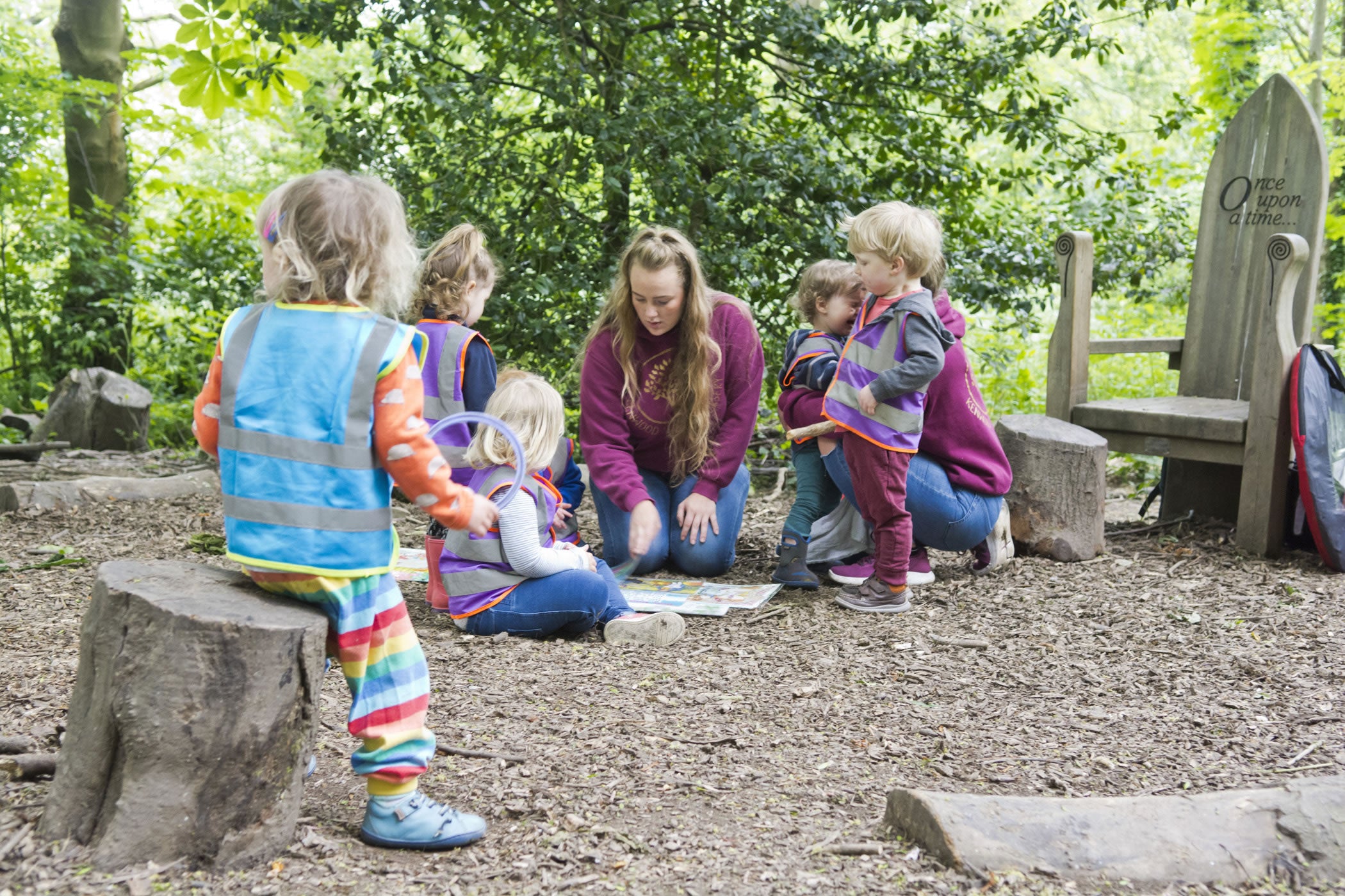 An adult sitting on the woodland floor among a group of small children