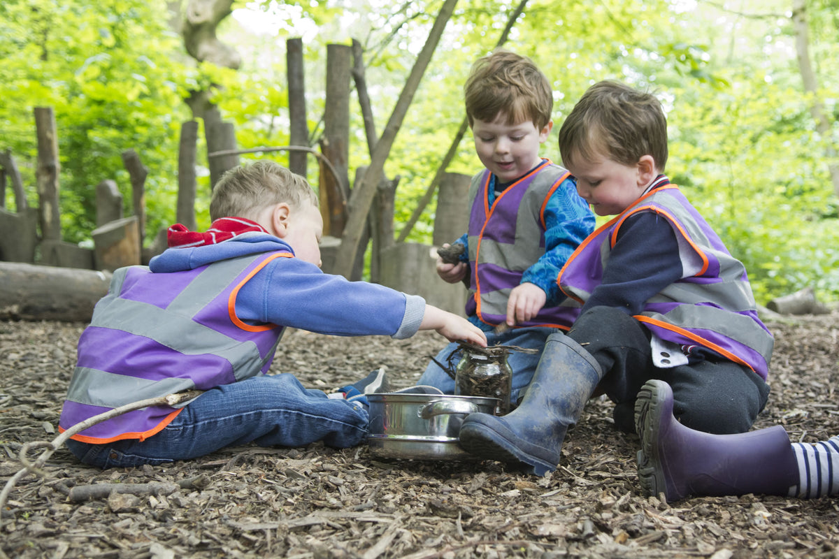 Two children crouched over a pan on the woodland floor, working it out between them