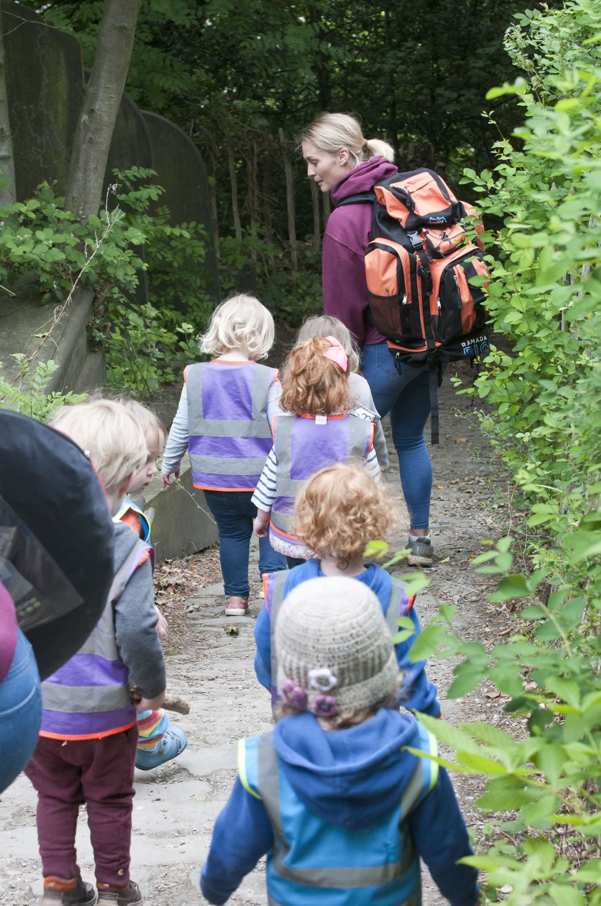 Children in high visibility vests walking into woodland with their practitioner
